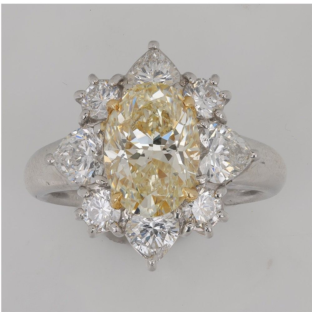 Studio source photo of a fancy yellow oval diamond cluster ring on a gray backdrop with dull metal