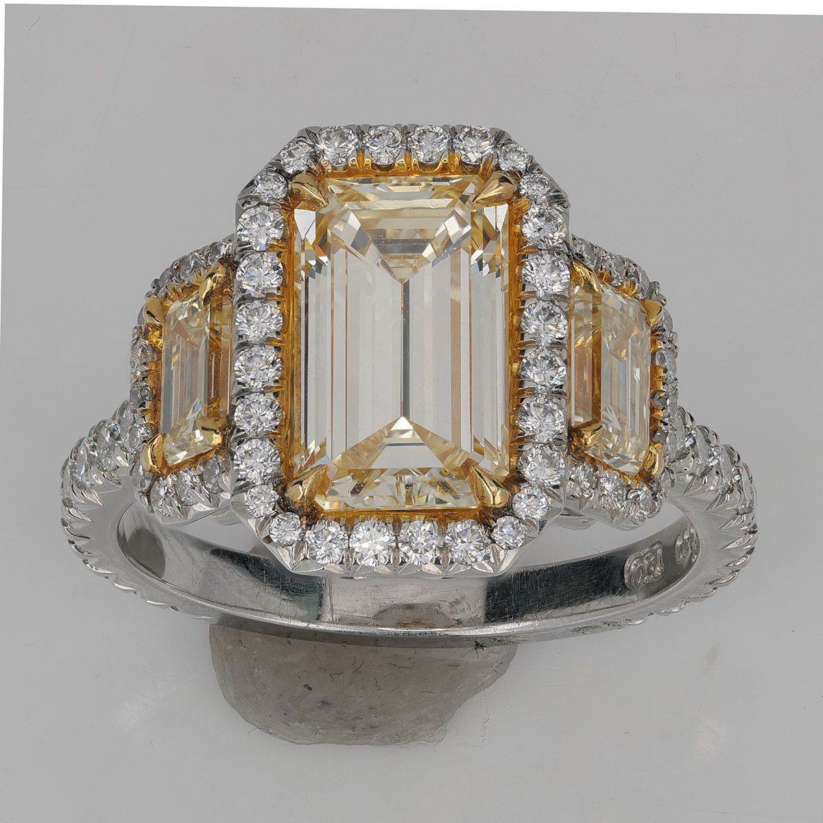 An emerald-cut yellow diamond three-stone ring retouched in NeuroViz — the metal and the background are cleaned, the stones are untouched.