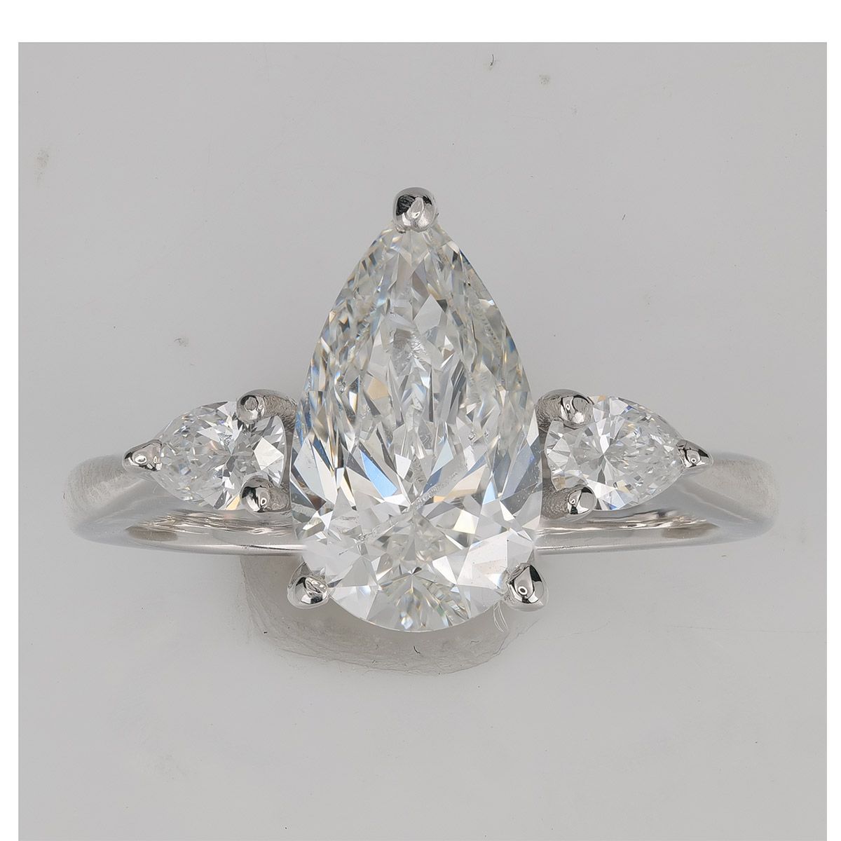 A pear-cut diamond before AI retouching — the facet pattern and the fire are identical in both shots; only the dust, the marks and the grey background are gone.